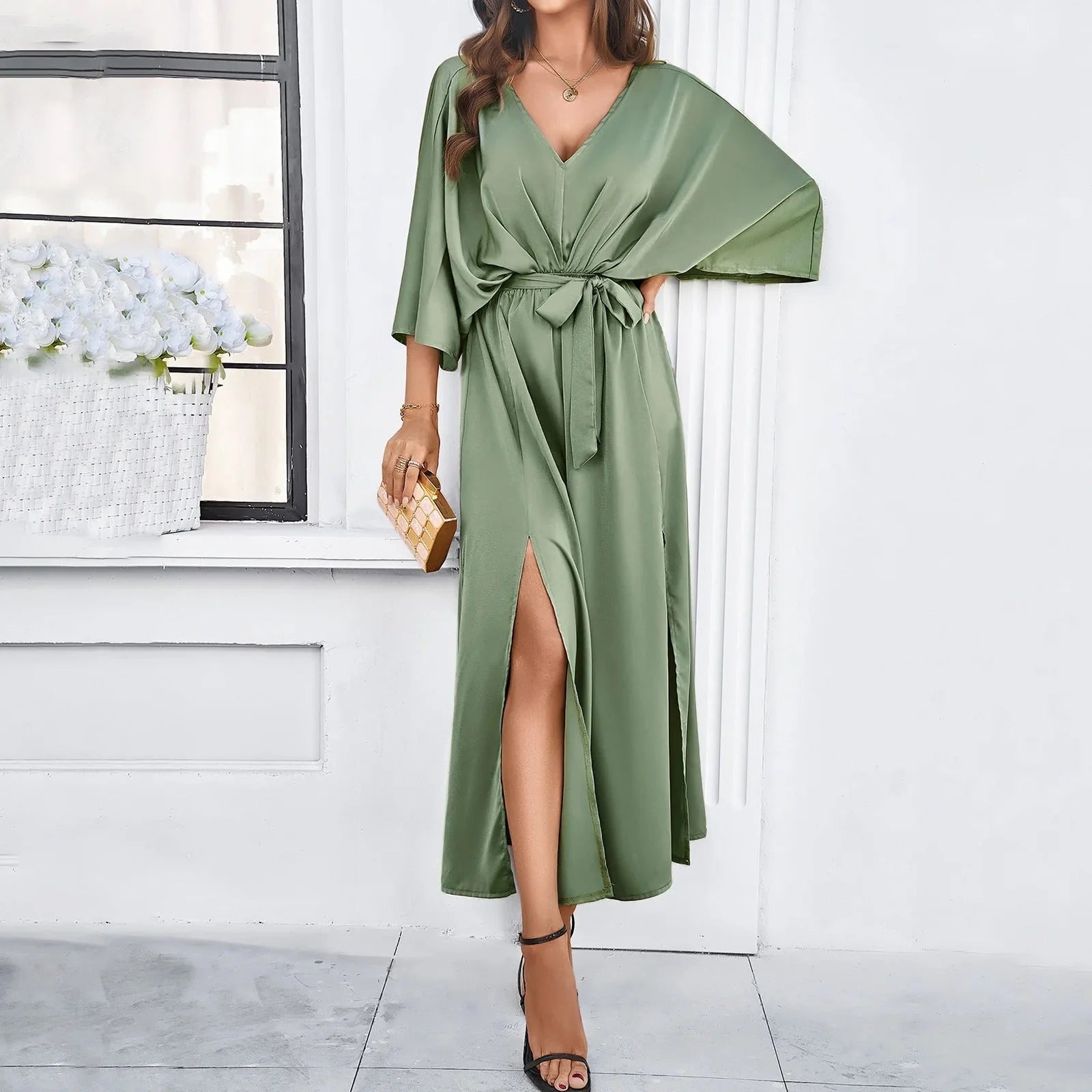 Model draagt beige maxi jurk met strikceintuur en strappy hakken voor elegante look