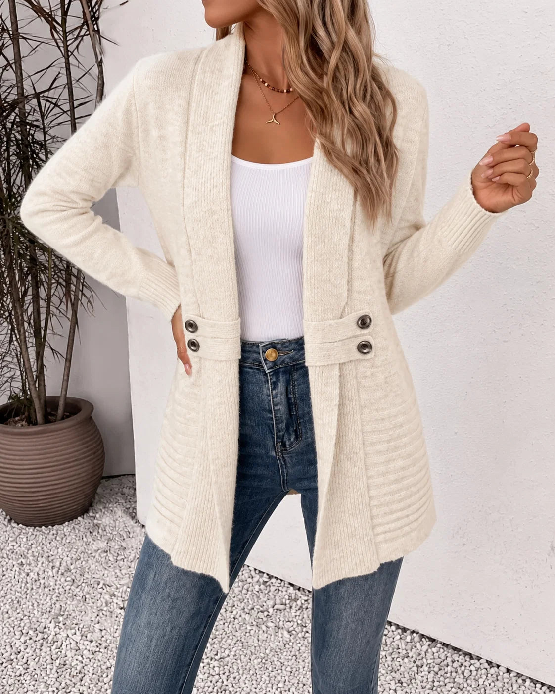 Close-up van gebreid vest met sjaalkraag en decoratieve knoopdetails bij de taille