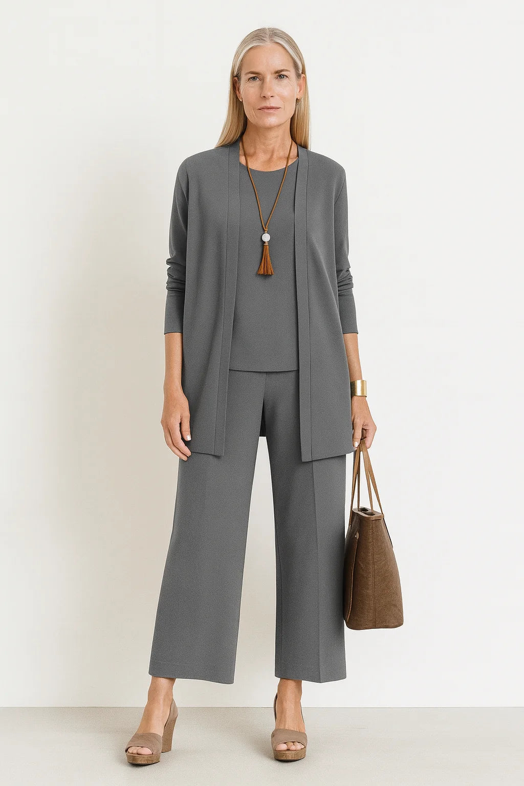 Vrouw draagt grijze driedelige set met lang vest, top en wijde broek in relaxed pasvorm