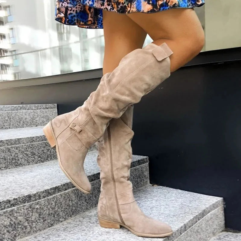 Dames kniehoge suède laarzen in beige met lage blokhak en rits sluiting gedragen op trap