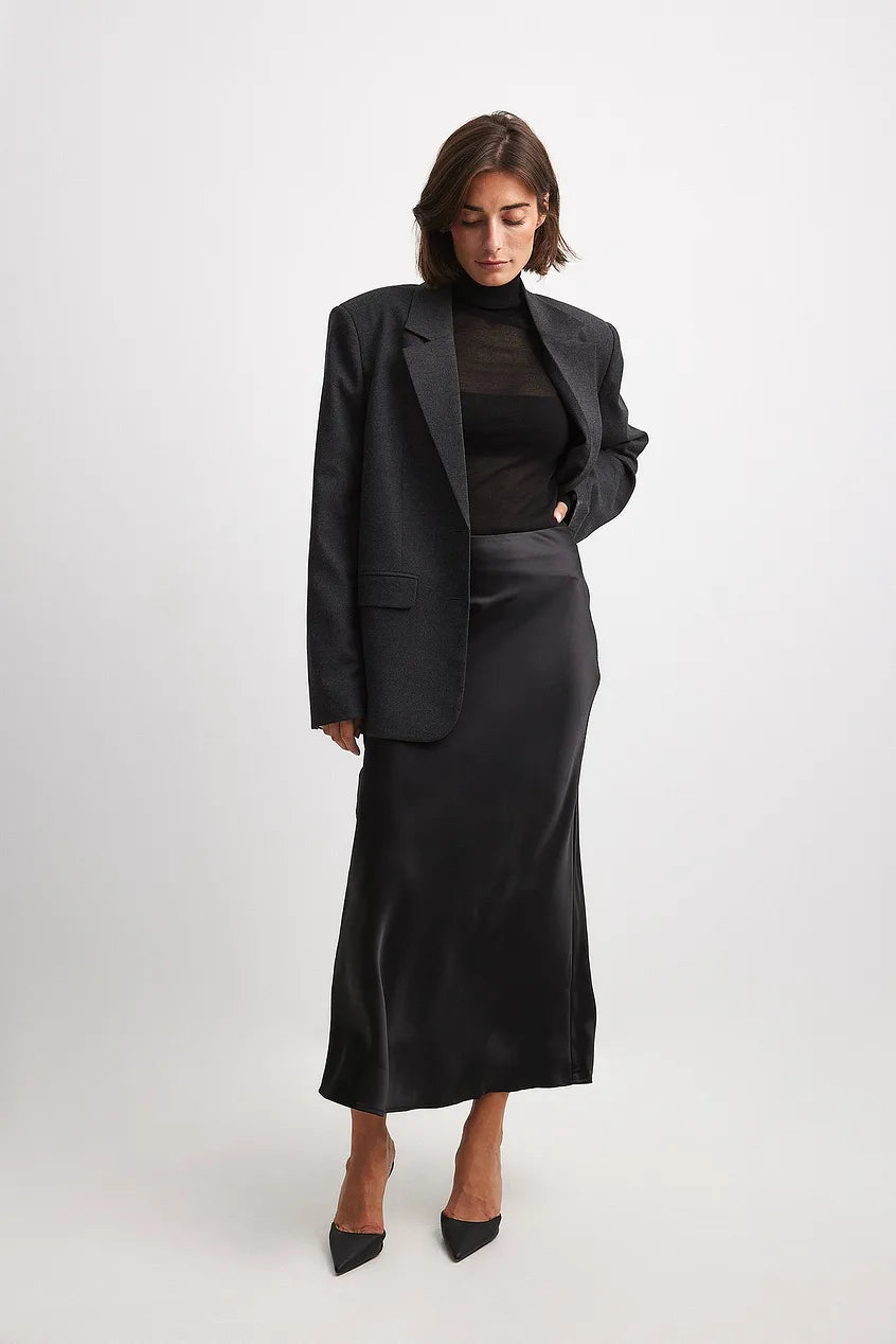 Vrouw draagt zwarte satijnen maxi rok met blazer en zwarte pumps voor een moderne look