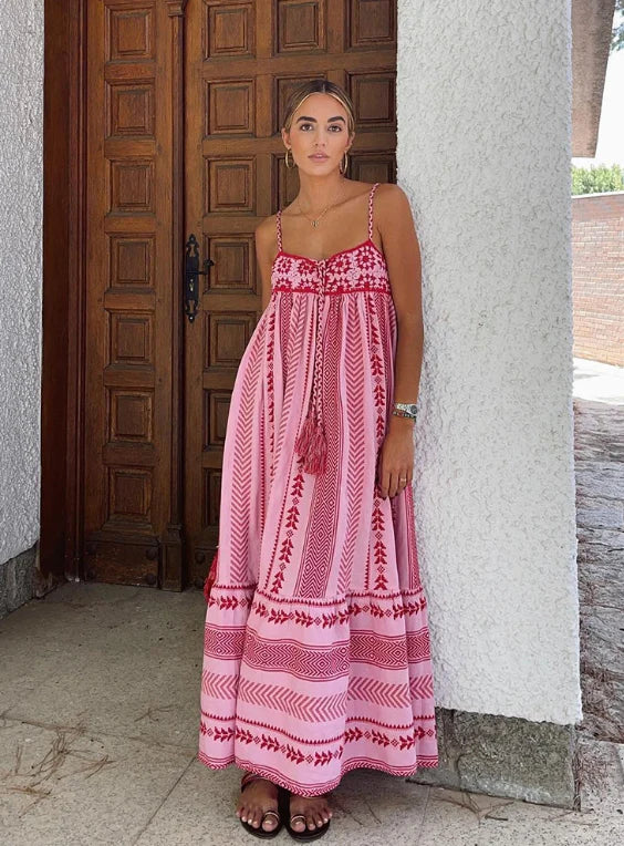 Vrouw draagt roze maxi zomerjurk met A-lijn pasvorm en decoratieve details bij deuropening