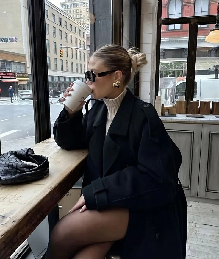 Vrouw in lange beige trenchcoat met zwarte pet en handtas