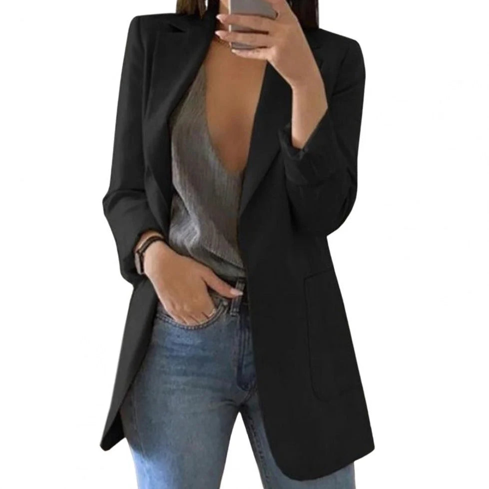 Vrouw draagt een zwarte lange blazer met klassieke revers en dubbele knoopsluiting over een grijze top en spijkerbroek