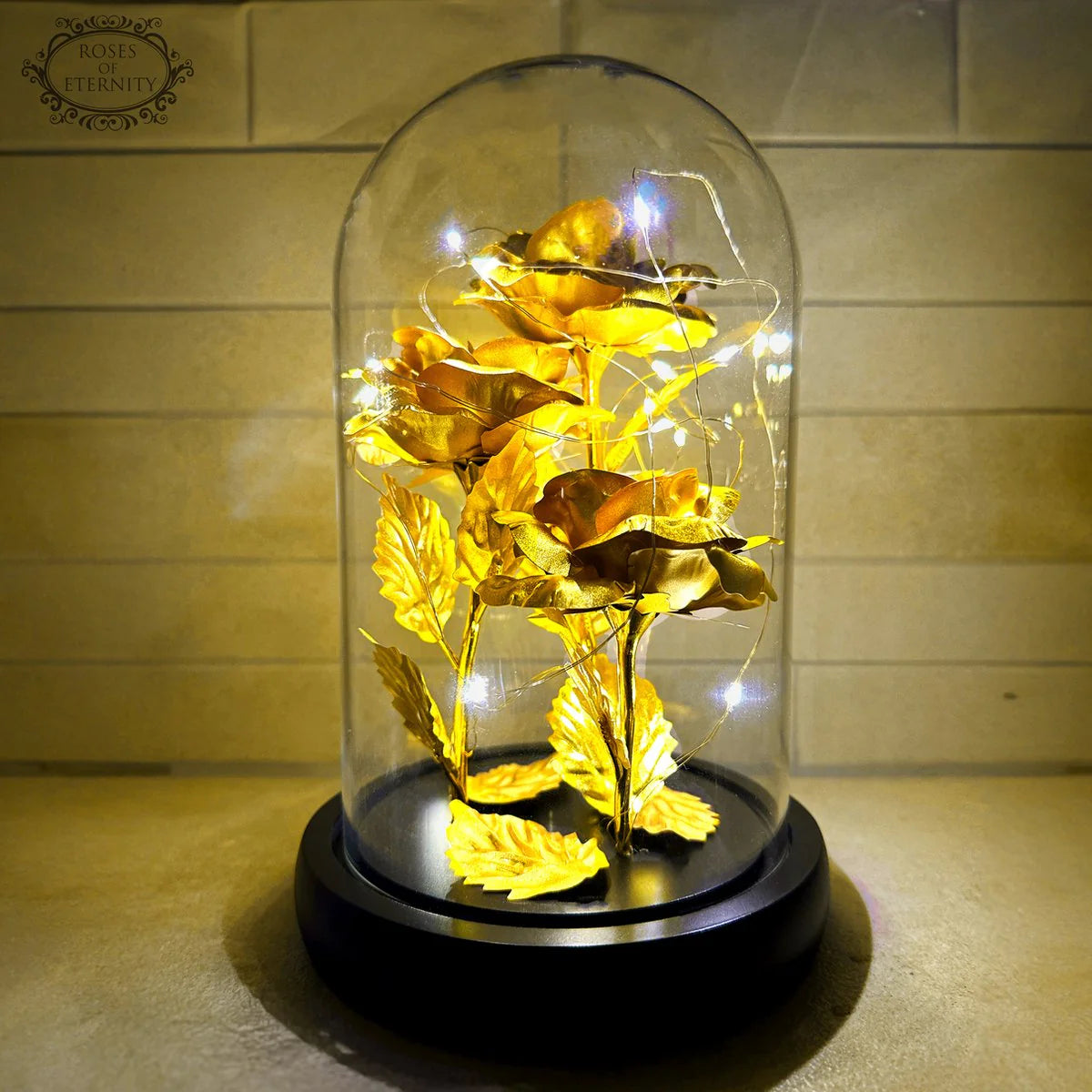Decoratieve roos met gouden bladeren en LED-verlichting in glazen stolp