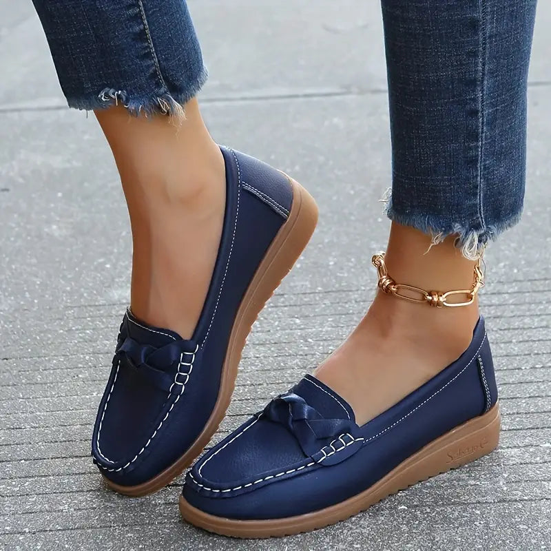 Dames loafers met strikdetail in marineblauw, gedragen met spijkerbroek en gouden armband op grijze stoep