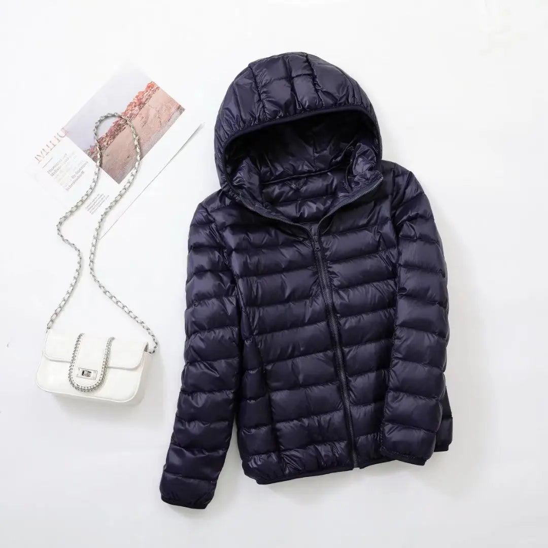 Marineblauw dames puffer jas met capuchon en gewatteerd ontwerp plat gelegd op witte achtergrond