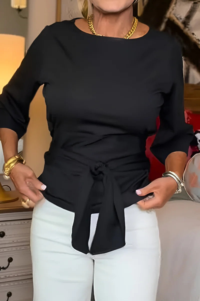 Vrouw draagt beige top met strik in de taille gecombineerd met witte broek
