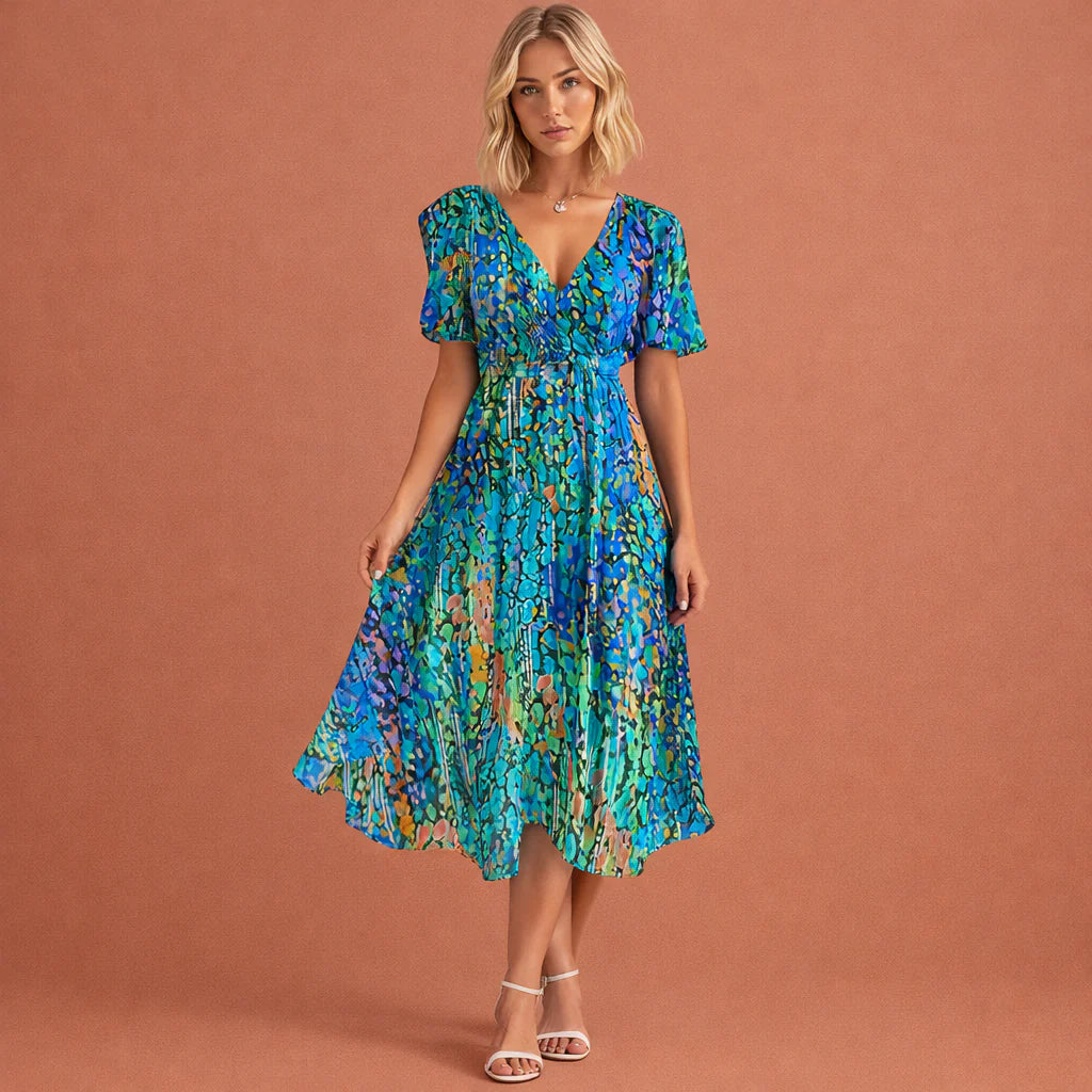 Vrouw draagt midi jurk met turkoois en blauwe bloemenprint en korte pofmouwen, V-hals en getailleerde pasvorm