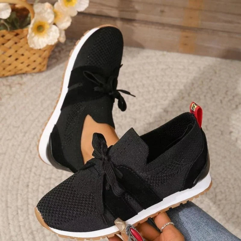 Zwarte gebreide dames sneakers met witte zool en rode hieldetail, vetersluiting zichtbaar