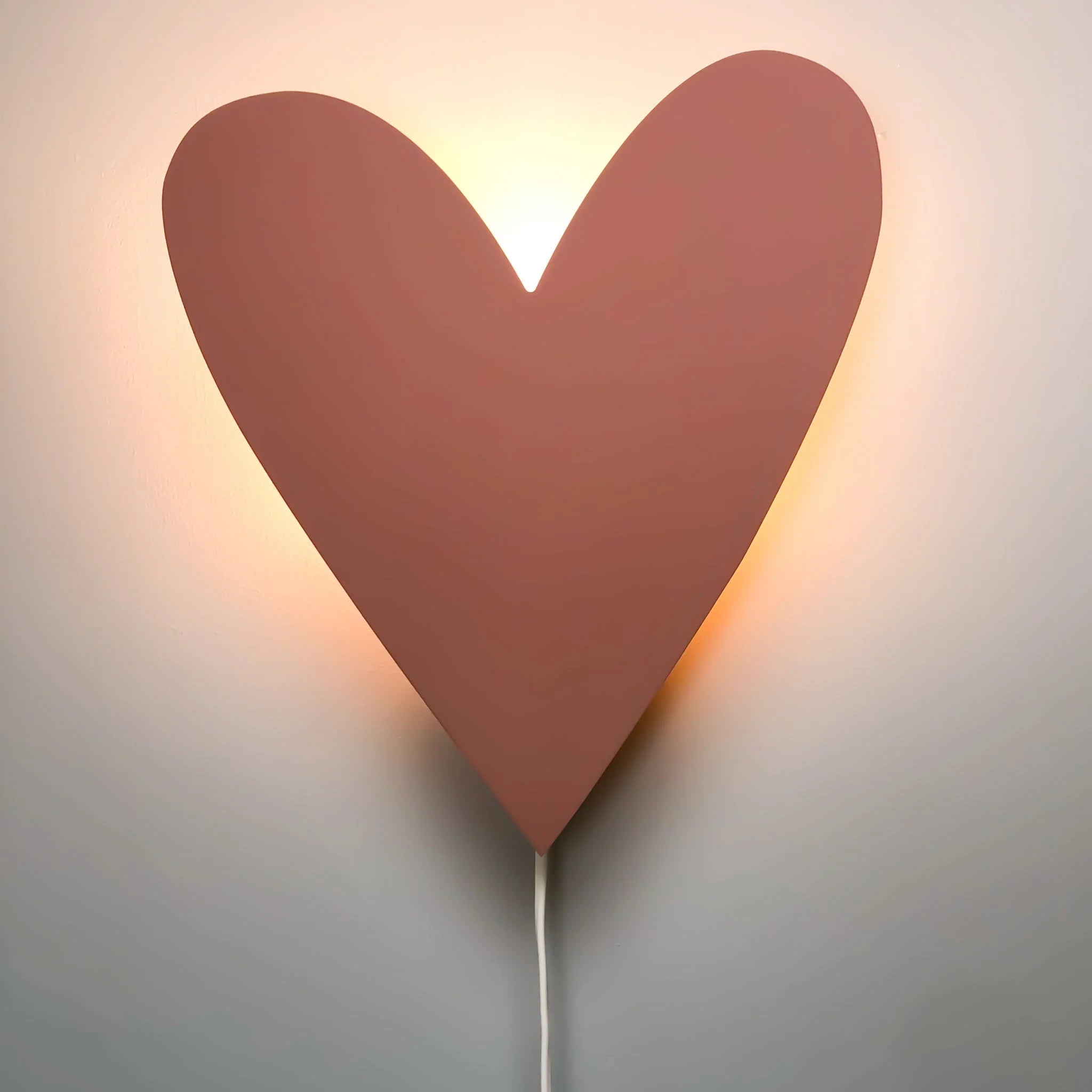 Hartvormige houten wandlamp in terra roze kleur gemonteerd tegen witte muur met zachte lichtgloed