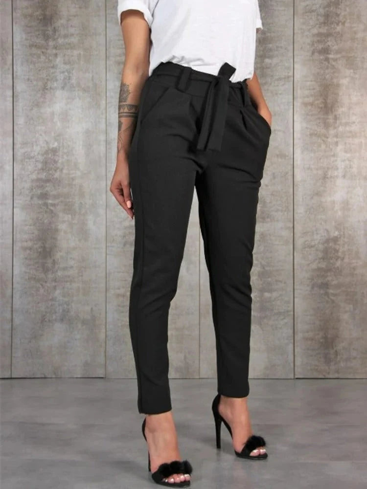 Zwarte dames paperbag broek met hoge taille en strikceintuur, gedragen met witte top en hakken