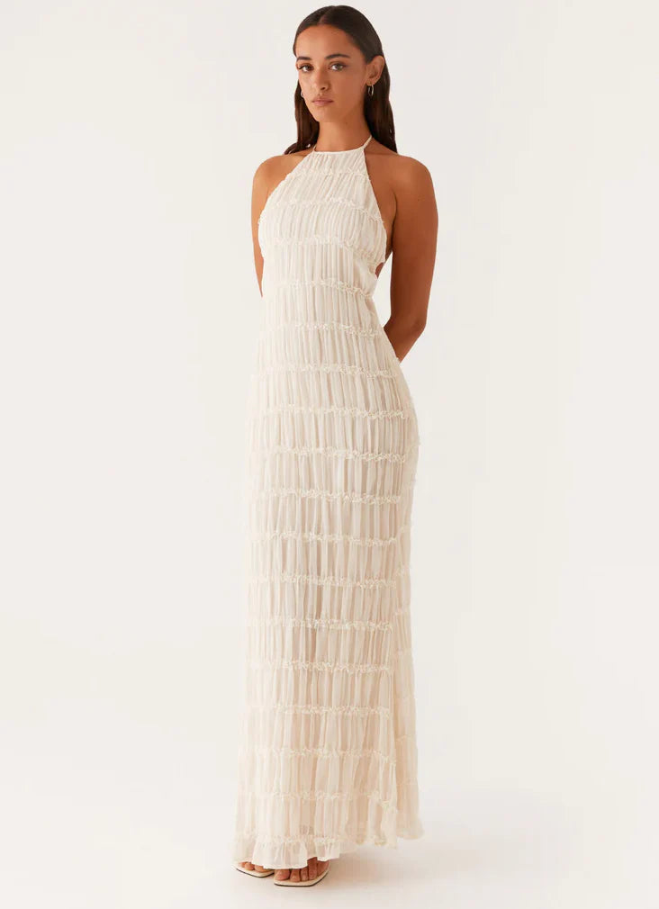 Vrouw draagt witte halter maxi jurk met gelaagde franjesdetails en verstelbare haltersluiting voor feestelijke gelegenheden