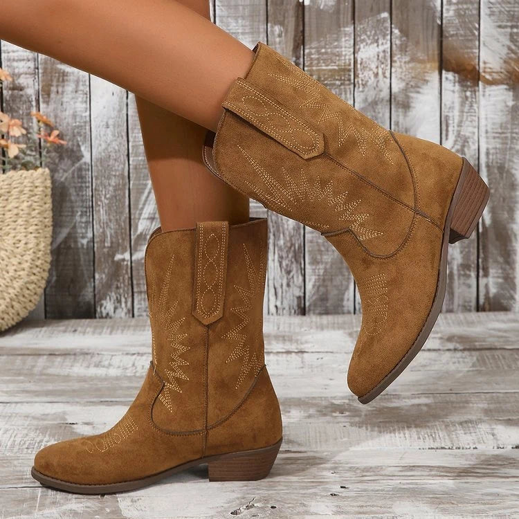 Lotje draagt bruine Dames Cowboy Enkellaarzen met western stiksels en middenhak op houten achtergrond