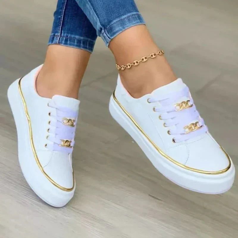 Zijaanzicht van zwarte platform sneakers met gouden rand en decoratieve kettingaccenten langs vetersluiting