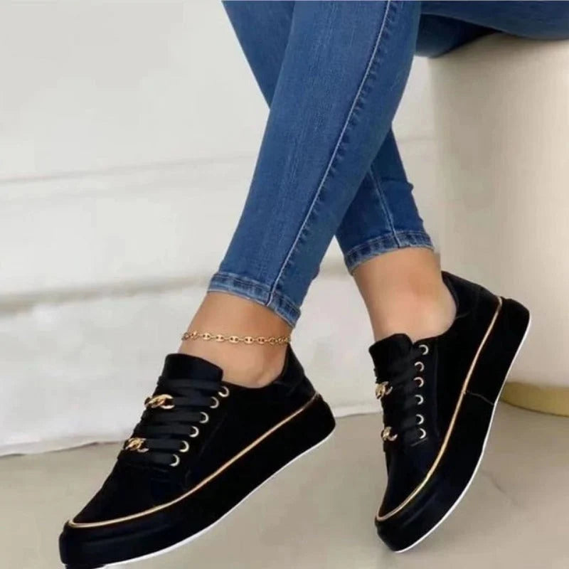 Detail van gouden kettingaccent en vetersluiting op zwarte dames platform sneakers