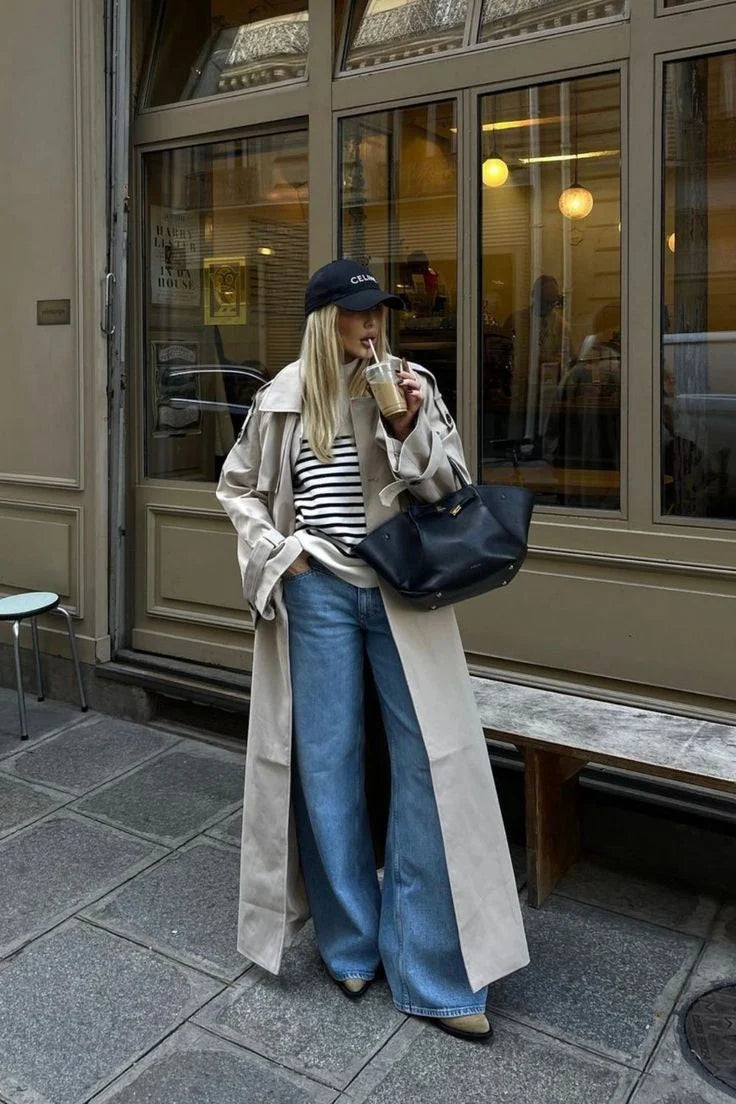 Vrouw draagt een beige lange trenchcoat met tailleband en gestreept shirt op straat