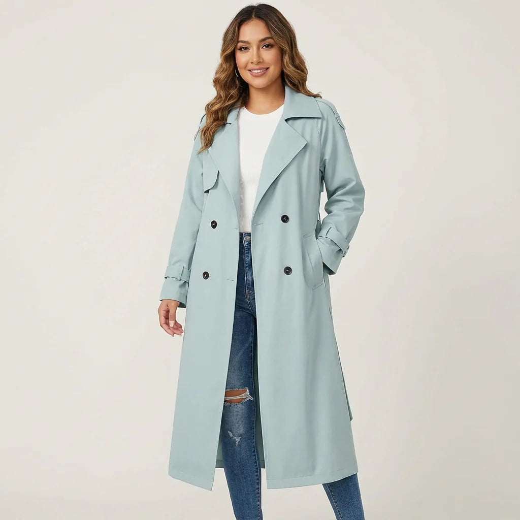 Vrouw draagt lange beige trenchcoat met klassieke knopenlijst gecombineerd met witte top en spijkerbroek