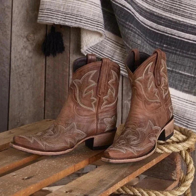 Dames cowboylaarzen in bruin leer met geborduurd Western-motief en blokhak op houten ondergrond