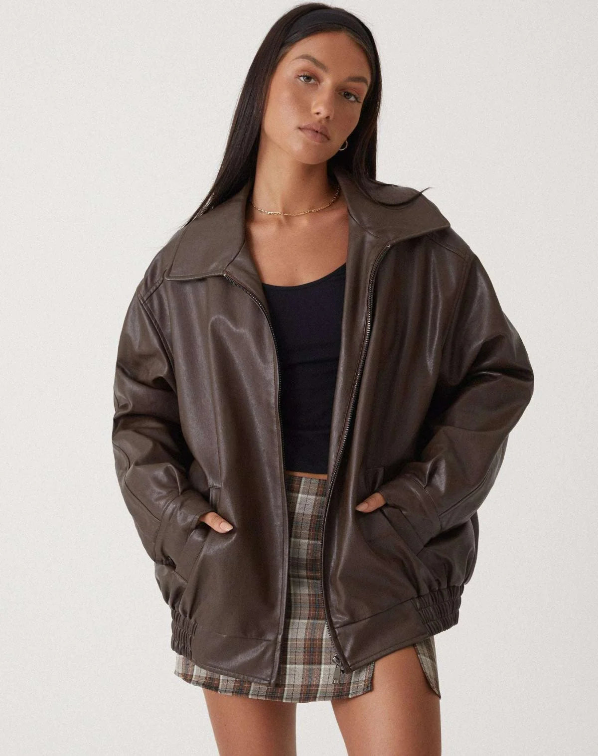 Dames oversized bomber jas in bruin met ritssluiting en elastische manchetten gedragen over zwarte top en geruite rok