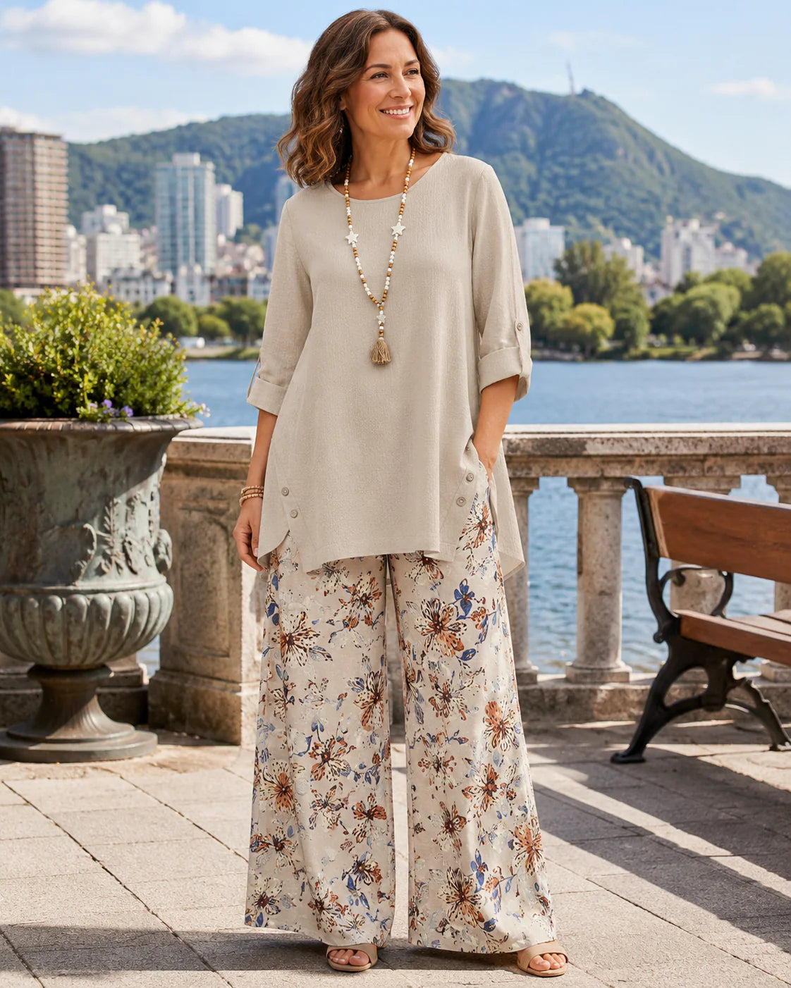 Dames tuniek set met wijde bloemenbroek in beige tinten, gedragen op zonnige buitenlocatie met waterachtergrond
