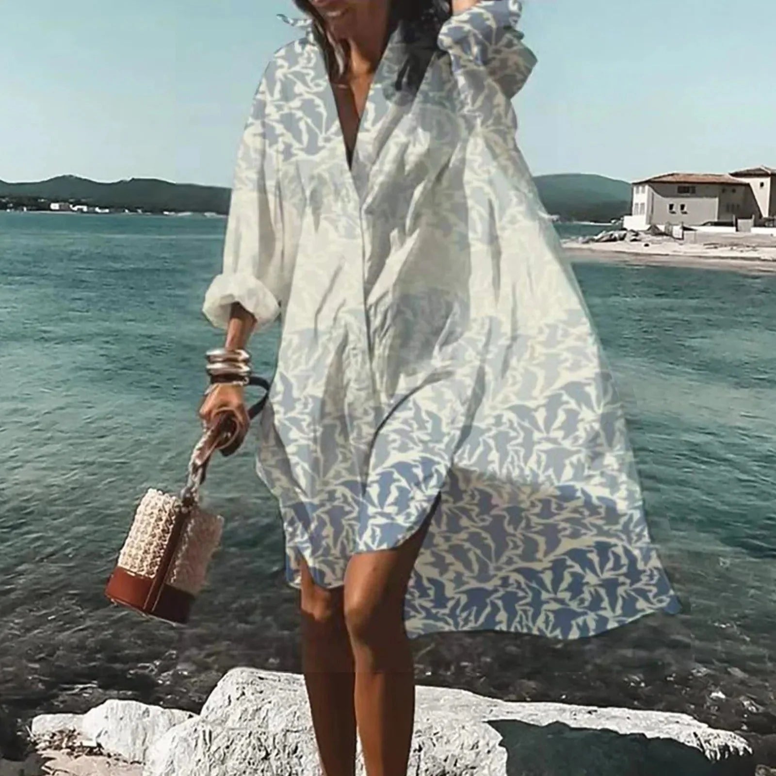 Vrouw draagt losse midi jurk met blauw-wit print en V-hals aan de kust