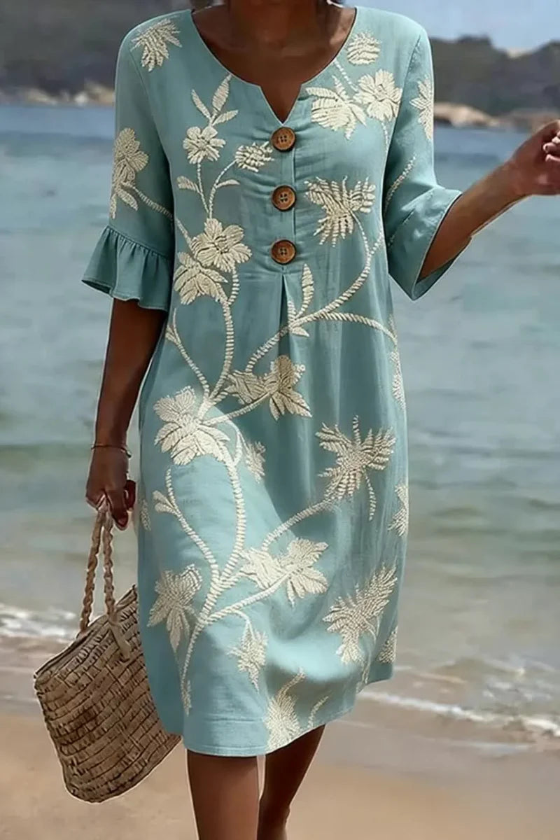 Midi jurk met geborduurde bloemen in lichtblauw, V-hals met knoopsluiting en ruche mouwen, gedragen op het strand