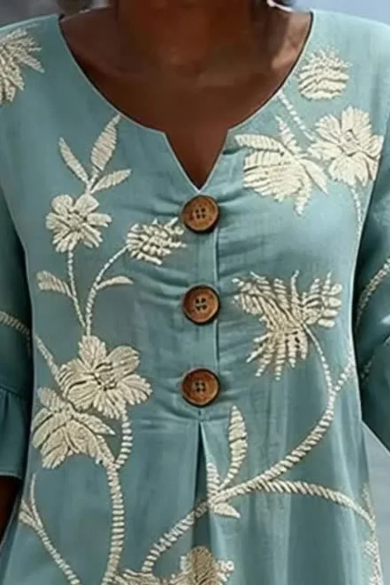 Detail van geborduurde bloemen op lichtblauwe midi jurk met knoopsluiting en ruche mouwen