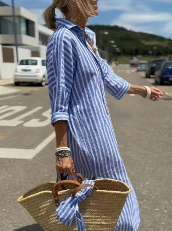 Gestreepte midi blousejurk met doorknoop sluiting en polokraag, gedragen met rieten tas in zomerse setting