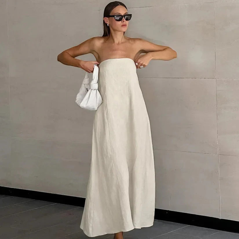 Vrouw draagt een witte strapless maxi jurk met los vallende pasvorm en minimalistische snit